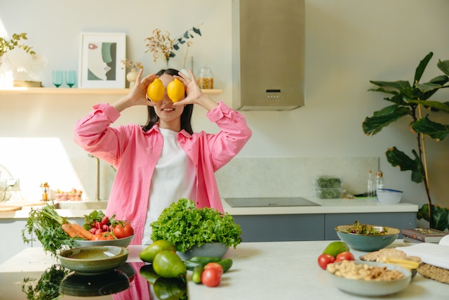 A woman in the kitchen holding lemons over her eyes